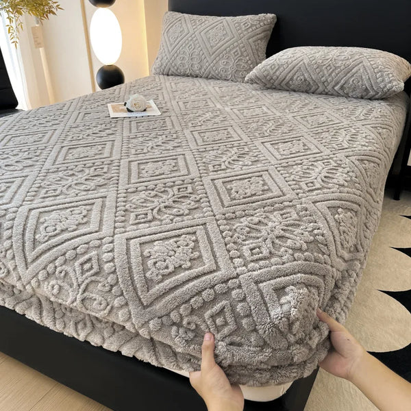 A gray warm plush mattress cover with an elastic edge is shown on a bed.