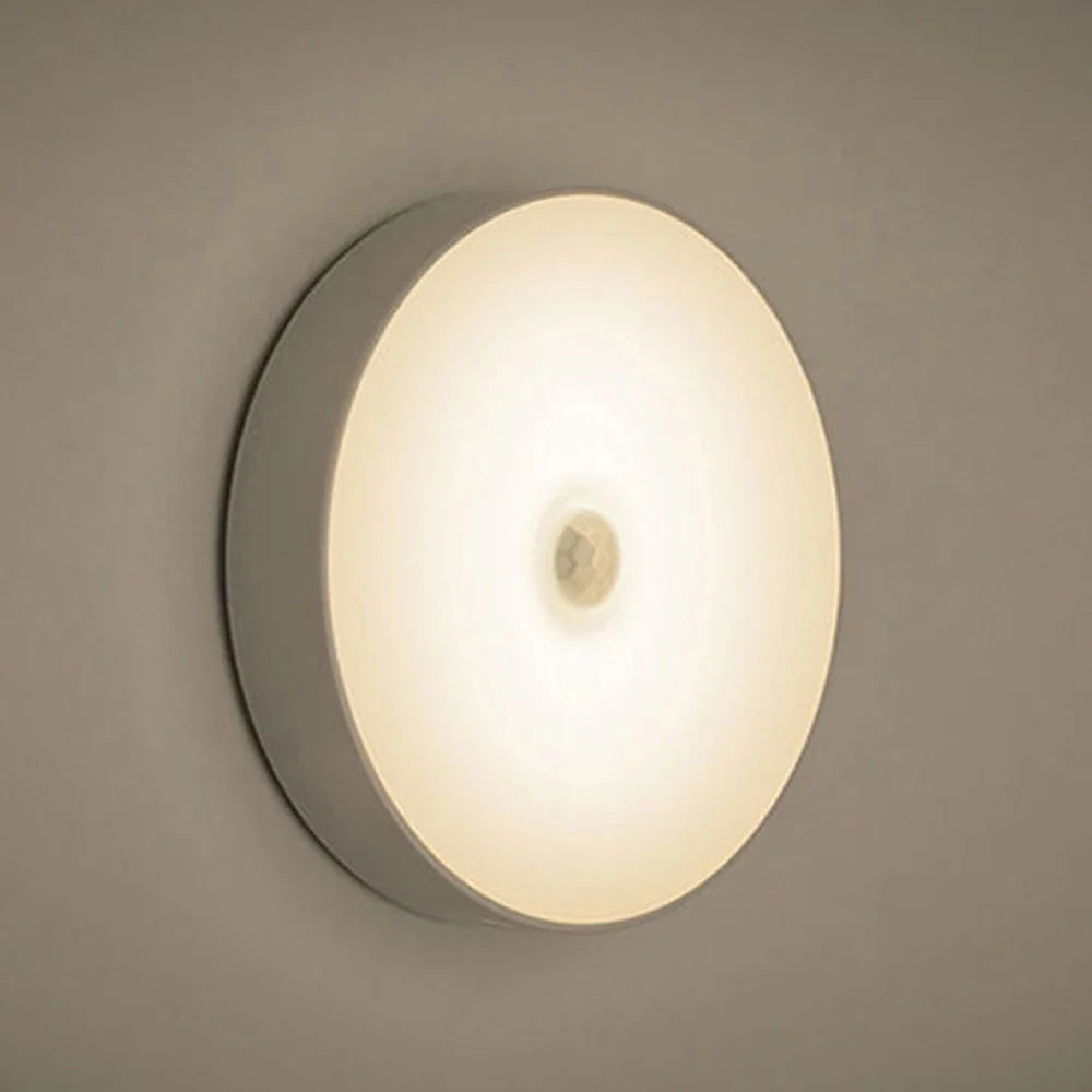 A round, flush-mounted magnetic LED night light with a soft white glow on a neutral wall.