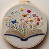 A circular embroidery piece featuring floral designs and an open book made of thread.
