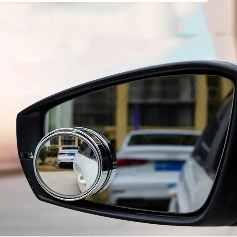 A close-up view of a black car mirror with a dual lens for blind spot visibility.