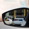 A close-up view of a black car mirror with dual lenses showing a reflection of a white car.