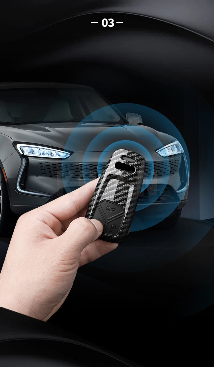 A hand holds a carbon fiber style key fob cover for an Audi car interior.