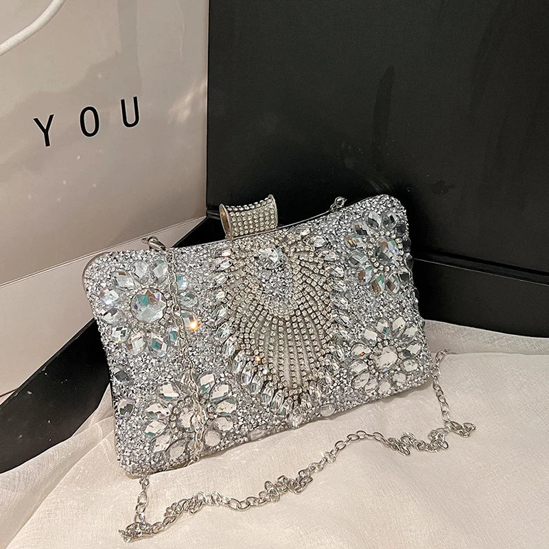 Silver rhinestone evening clutch with a decorative clasp and chain resting on a white surface.