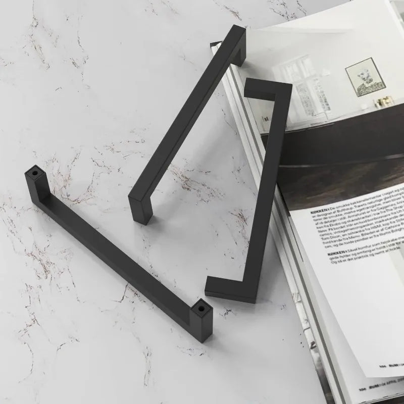 Matte black stainless steel cabinet pulls in a modern, angled design against a white marble background.