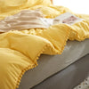 Yellow duvet cover set with pom-pom trim displayed on a bed.