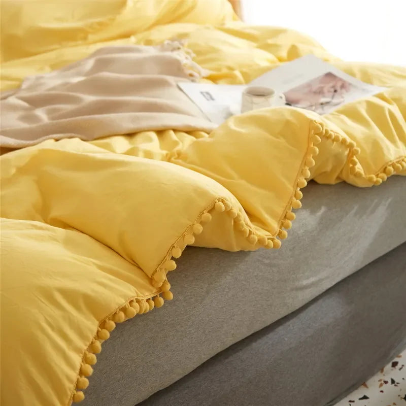 Yellow duvet cover set with pom-pom trim displayed on a bed.