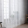 White sheer voile curtain panels with delicate silver embroidery hanging in a window.