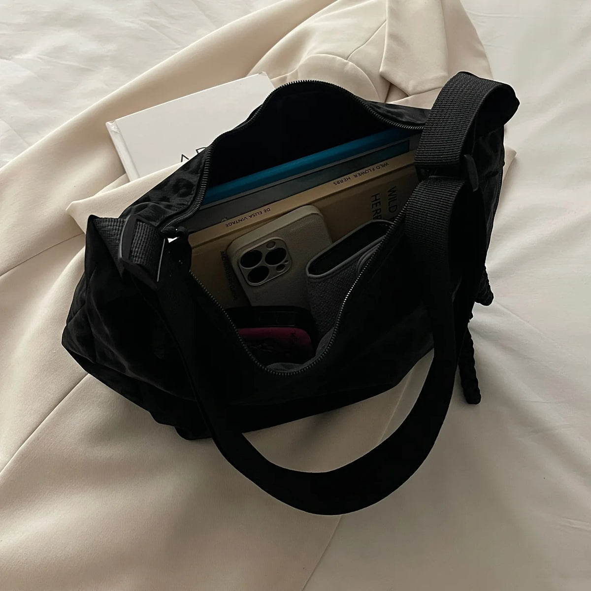 A black leopard print crossbody bag with various items inside, resting on a white sheet.