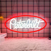 A neon sign shaped like the word Peterbilt is displayed against a pink tiled wall with a white fluffy rug.