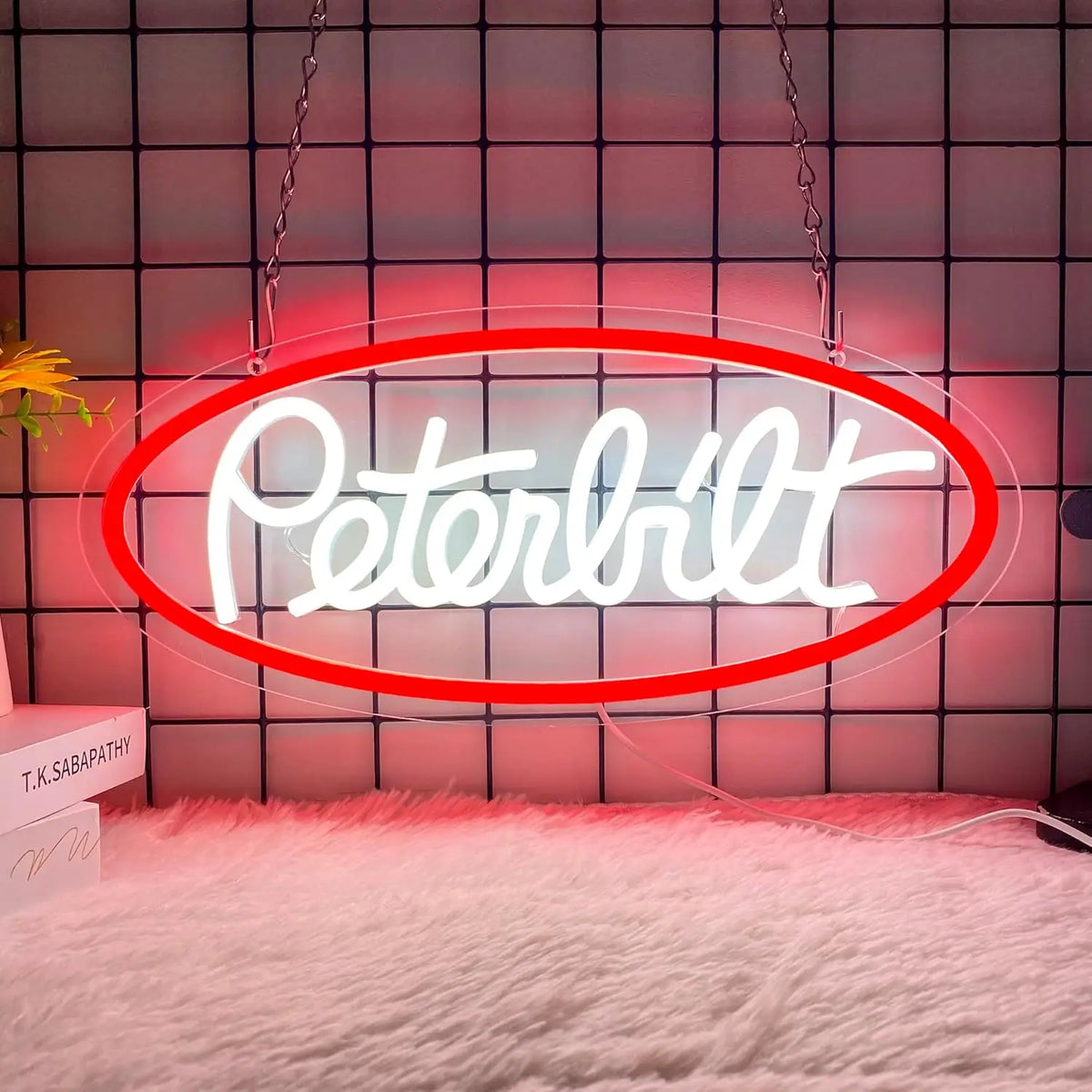 A neon sign shaped like the word Peterbilt is displayed against a pink tiled wall with a white fluffy rug.