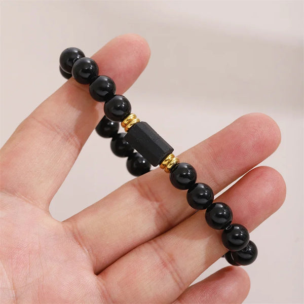 A hand holds a black tourmaline bracelet featuring spherical black beads and gold accents.