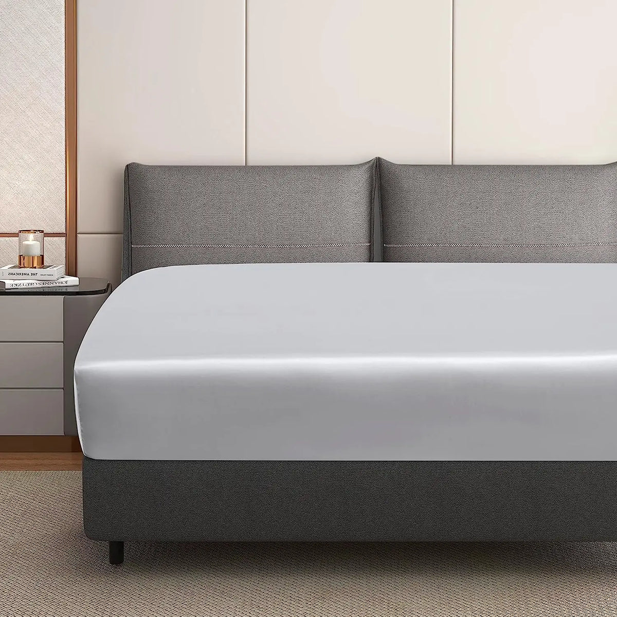 A luxury satin fitted sheet is displayed on a bed with gray bedding and light wood accents.
