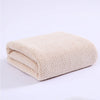 A beige knitted bath towel folded neatly on a white surface.