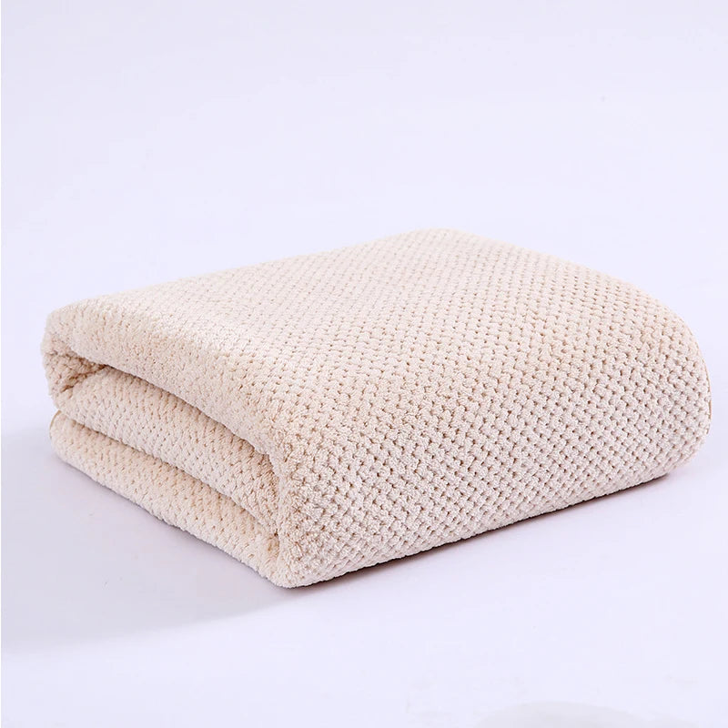 A beige knitted bath towel folded neatly on a white surface.