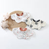 A collection of light-colored cotton baby feeding bibs and a woven mat are displayed on a white background.