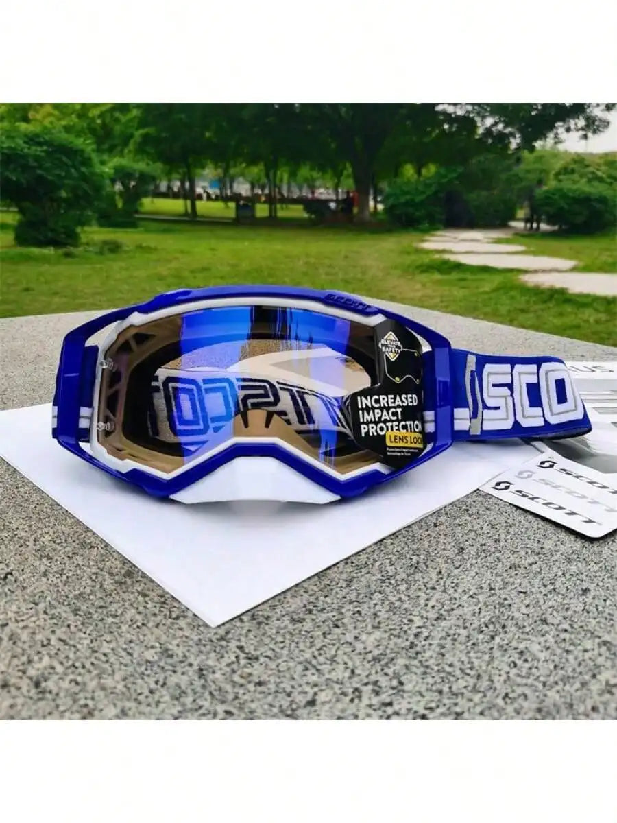 Blue and black motocross goggles resting on a gray surface with a blurred green outdoor background.
