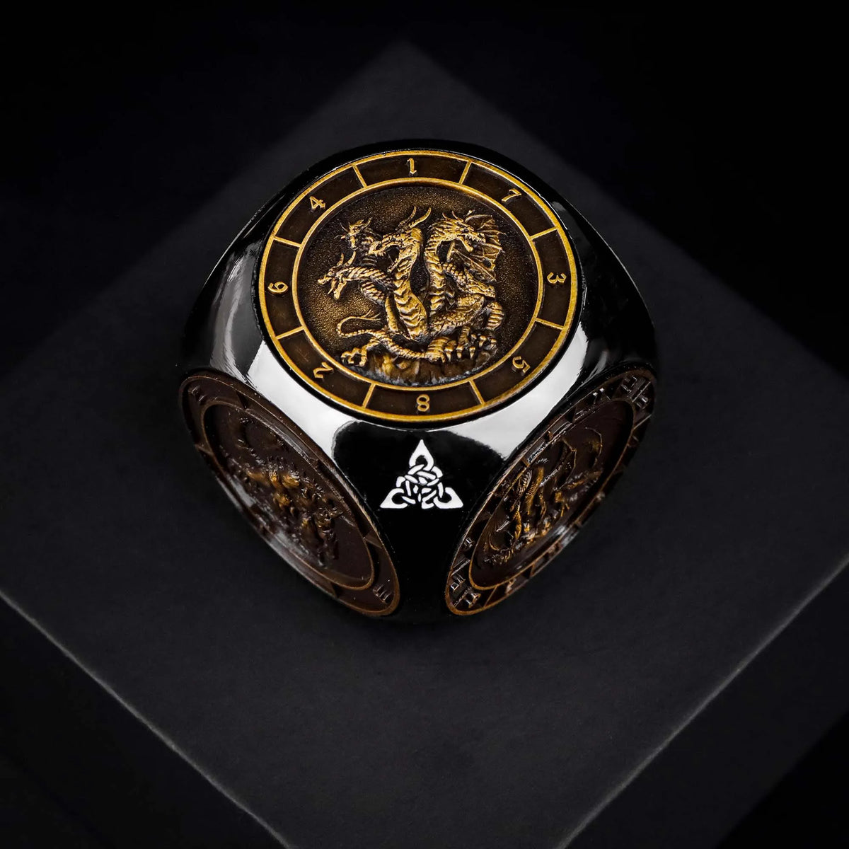 A black metal spinner dice cube featuring a gold-colored dragon design and a visible pentagram symbol.