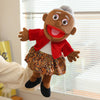 A soft plush full-body hand puppet resembling an elderly woman with gray hair, wearing a red jacket and patterned skirt.