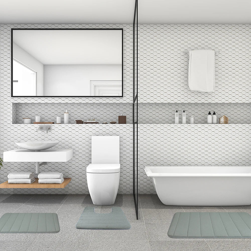 A modern bathroom featuring a white toilet, vanity, and bathtub with matching gray bath mats.