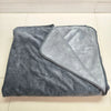 A folded gray flannel blanket with a lighter gray reversible side resting on a white tiled floor.