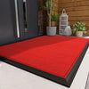 A bright red non-slip doormat placed on a light gray floor in front of a dark door with potted plants.