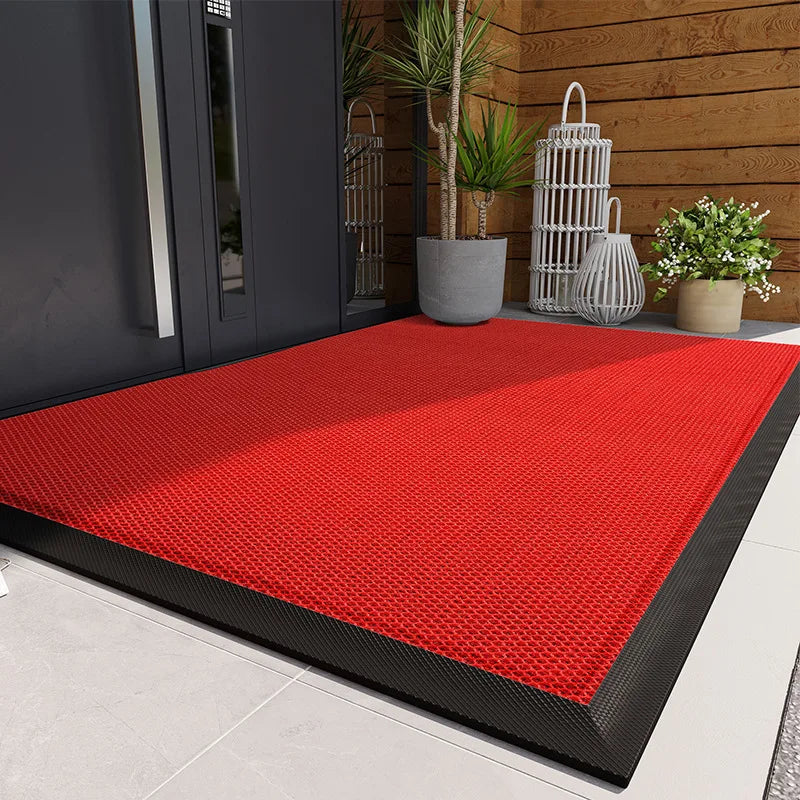 A bright red non-slip doormat placed on a light gray floor in front of a dark door with potted plants.