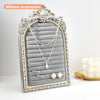 Silver arched resin jewelry display stand with a floral design featuring a silver necklace and earrings.