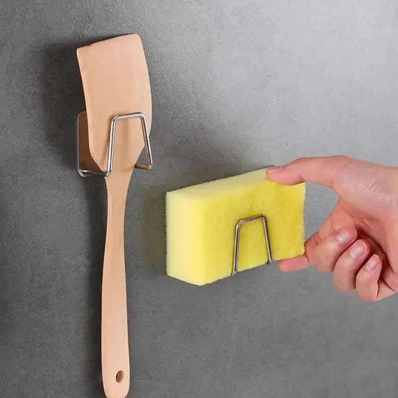 A hand is holding a light yellow sponge holder with a stainless steel frame against a gray wall.
