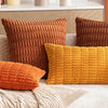 A set of three textured corduroy throw pillows in shades of burnt orange, mustard yellow, and deep brown on a light sofa.