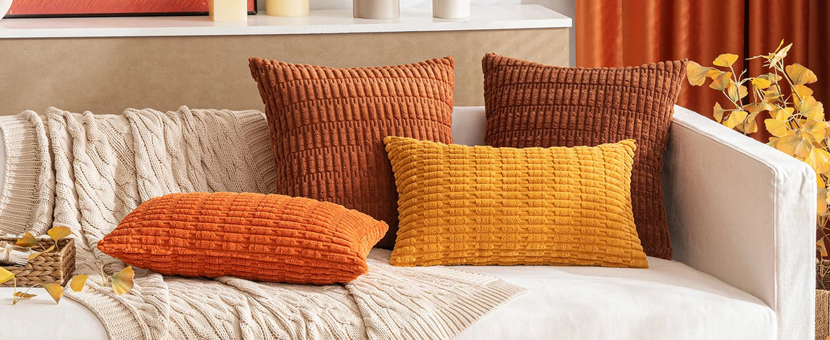 A set of three textured corduroy throw pillows in shades of burnt orange, mustard yellow, and deep brown on a light sofa.