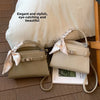 Beige PU-Leder-Clutchtasche mit Satinband auf Holzfußboden neben weißem Kissen.