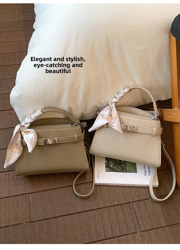 Beige PU-Leder-Clutchtasche mit Satinband auf Holzfußboden neben weißem Kissen.