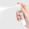 A hand is spraying a fine mist of white liquid from a clear plastic refillable spray bottle.