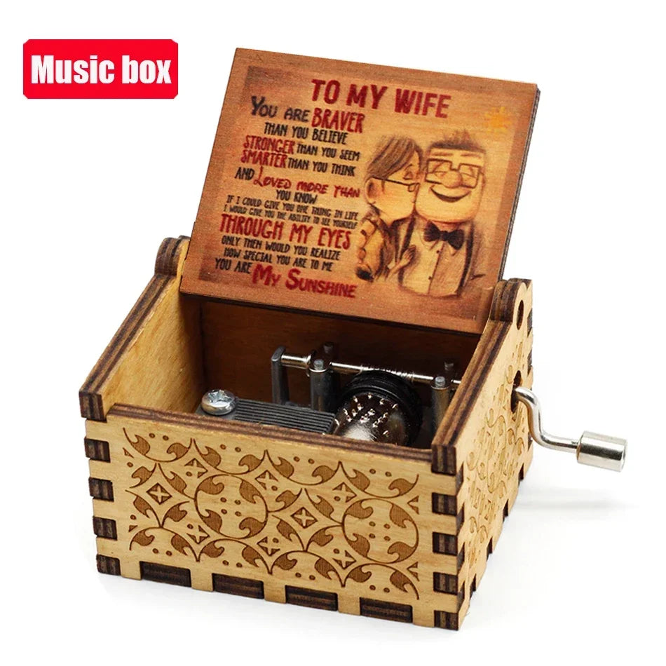 A vintage hand-crank wooden music box with an engraved lid featuring the text You Are Braver Than You Believe and a smiling i