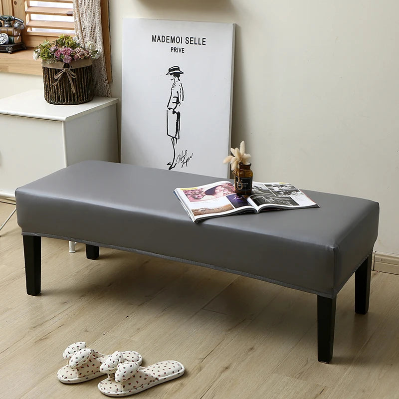 A gray waterproof PU stretch bench cover is displayed on a wooden floor next to a framed illustration.