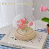 A handcrafted pink tulip LED night light with a clear glass dome and wooden base resting on a book.
