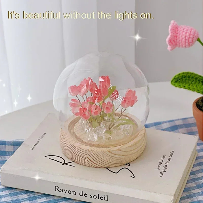 A handcrafted pink tulip LED night light with a clear glass dome and wooden base resting on a book.