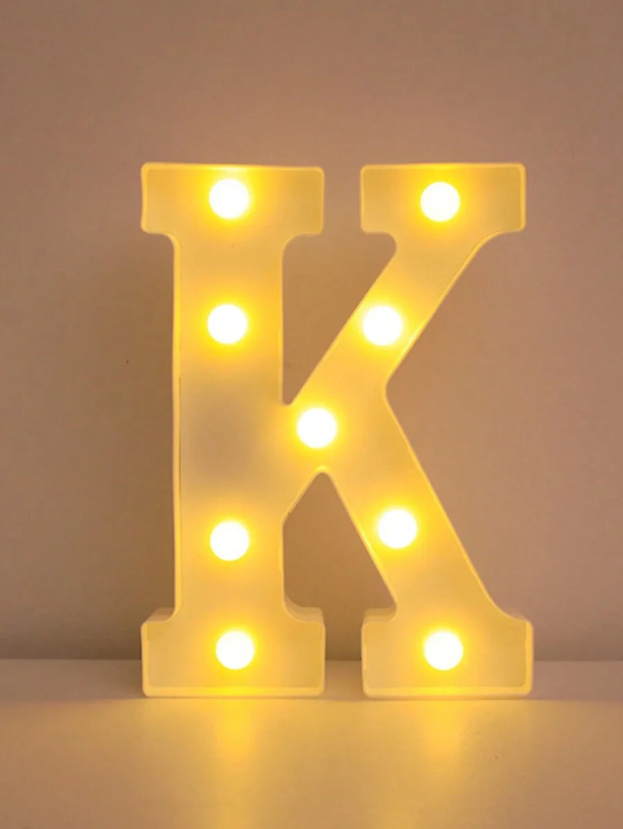 A glowing yellow LED letter K sign made of light bulbs used for home and party decor.