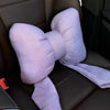 A lavender butterfly bow tie neck pillow with a soft fabric cover resting on a dark leather seat.