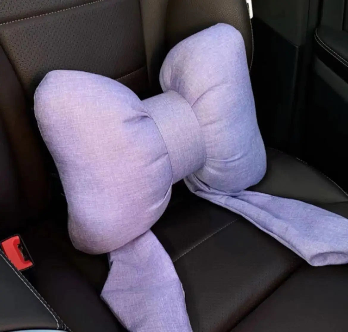 A lavender butterfly bow tie neck pillow with a soft fabric cover resting on a dark leather seat.