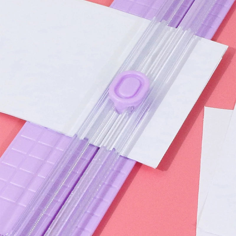 Un coupe-papier manuel portable avec une cutter en plastique violet sur un fond rose.