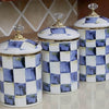 Three white porcelain storage jars with blue and yellow checkerboard patterns and gold lids