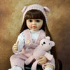 A lifelike silicone baby doll wearing a pink knitted hat and overalls, holding a small pink stuffed animal.
