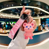 A hand holds a pink plush toy shaped like a rabbit, attached to a black leather key case.
