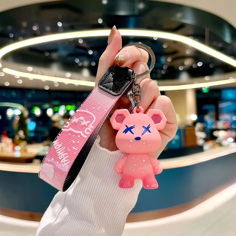 A hand holds a pink plush toy shaped like a rabbit, attached to a black leather key case.