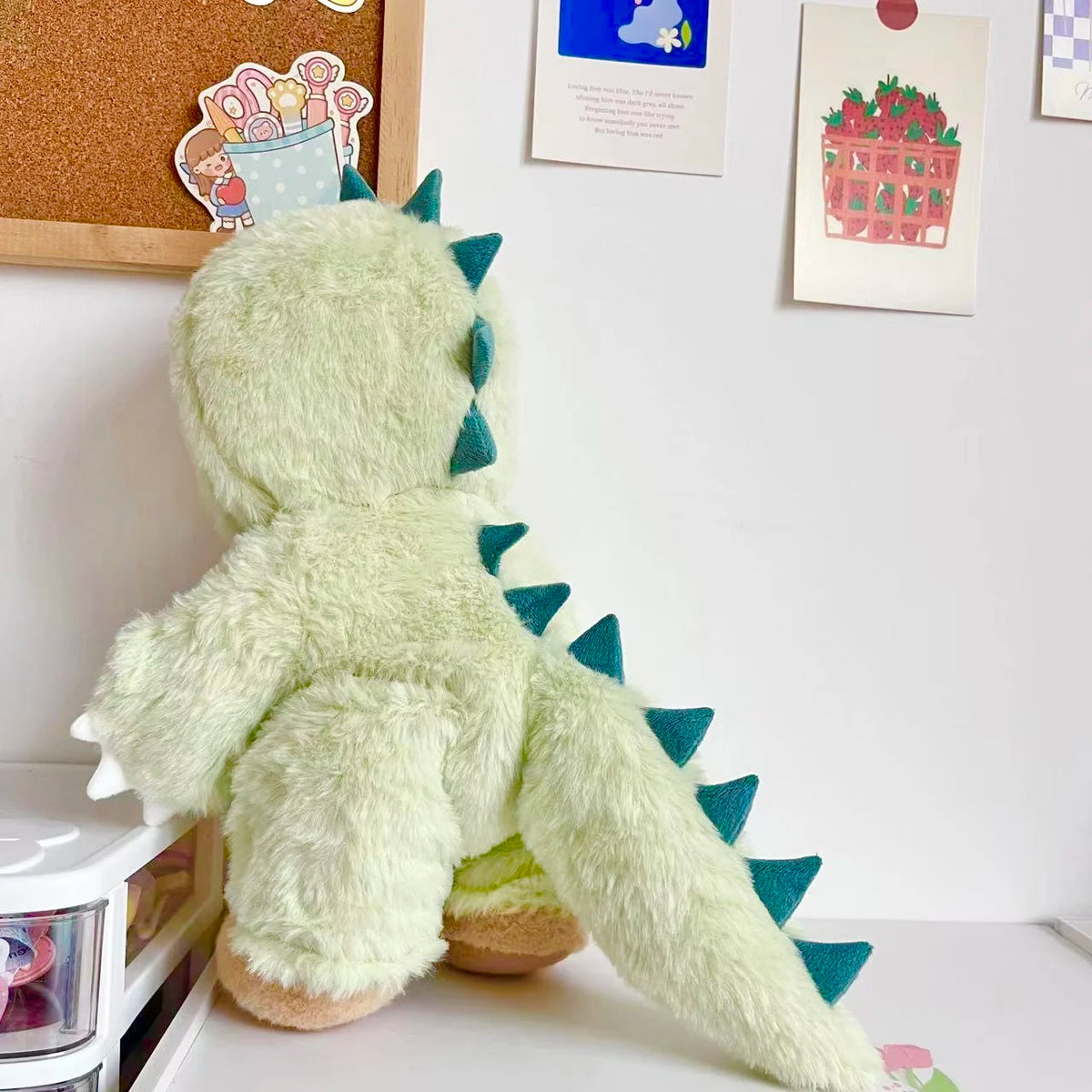 A light green dinosaur plush toy wearing a matching outfit, sitting on a white surface.