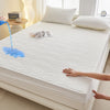 A white fitted mattress protector is shown with a blue liquid dripping onto the surface.