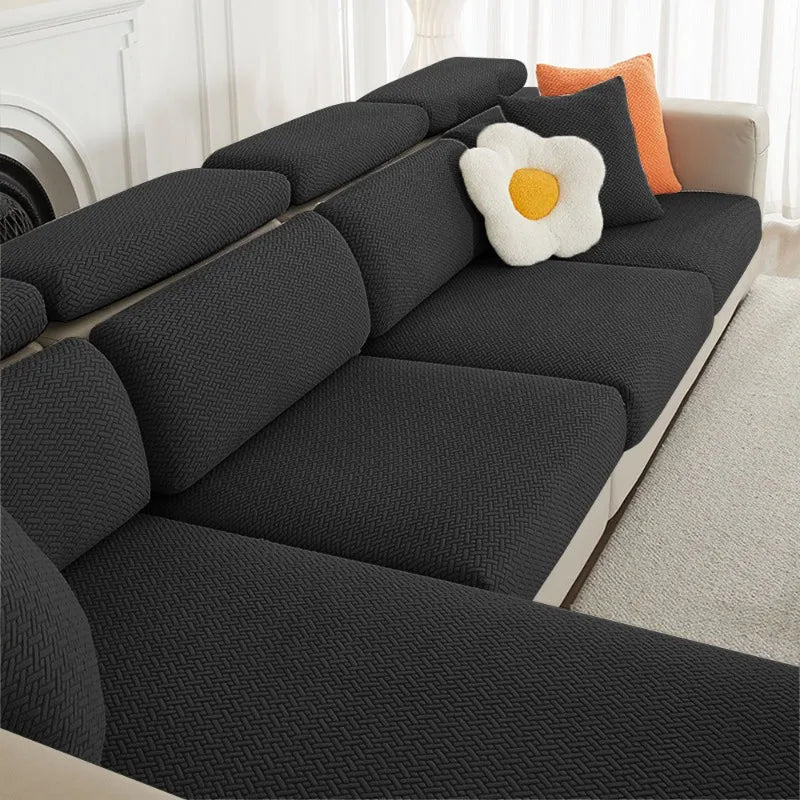 A dark gray jacquard elastic sofa slipcover with orange and white accent pillows.