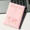 Pinkes Reisepasshülle mit Weltkarte auf weißer Fläche neben Laptop-Tastatur.