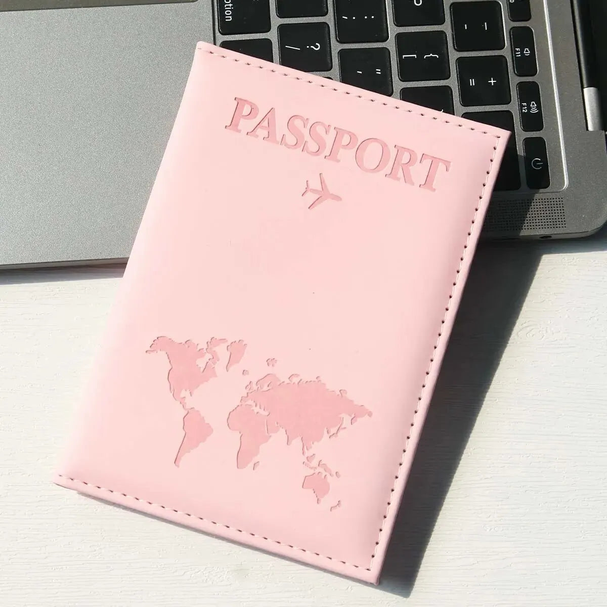 Pinkes Reisepasshülle mit Weltkarte auf weißer Fläche neben Laptop-Tastatur.